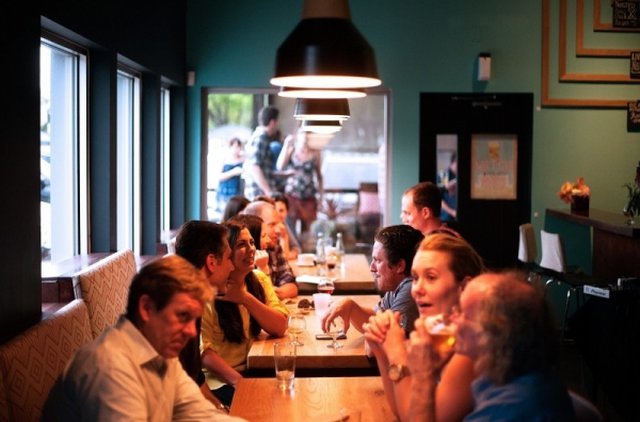 obrazek przedstawia rozmawiających ludzi w restauracji, którzy siedzą przy stolikach