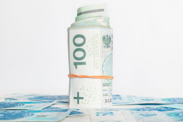 obrazek przedstawia zwinięty plik banknotów stu złotowych